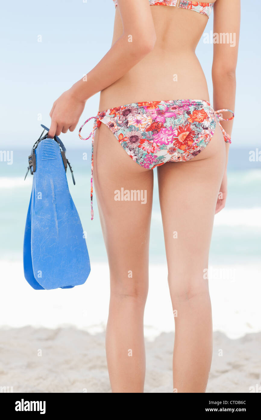 Woman in a bikini with her body slightly turned to the side holding a pair of flippers Stock Photo