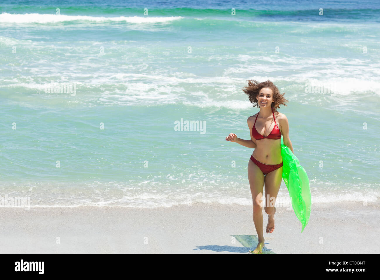 Woman in a bikini running while carrying a air bed Stock Photo