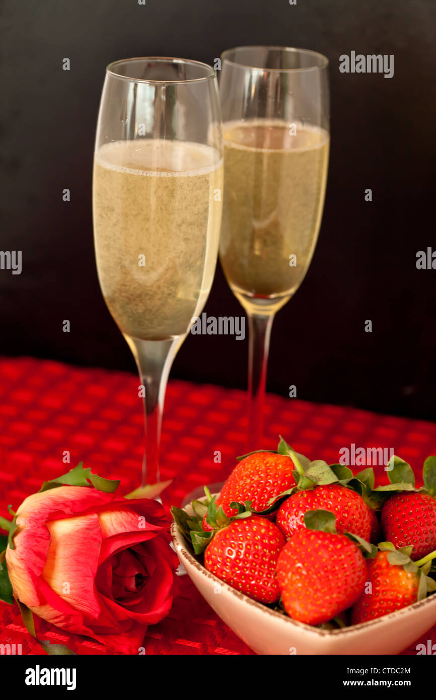 Top glasses of champagne with strawberries in a bowl and a rose on a red tablecloth Stock Photo