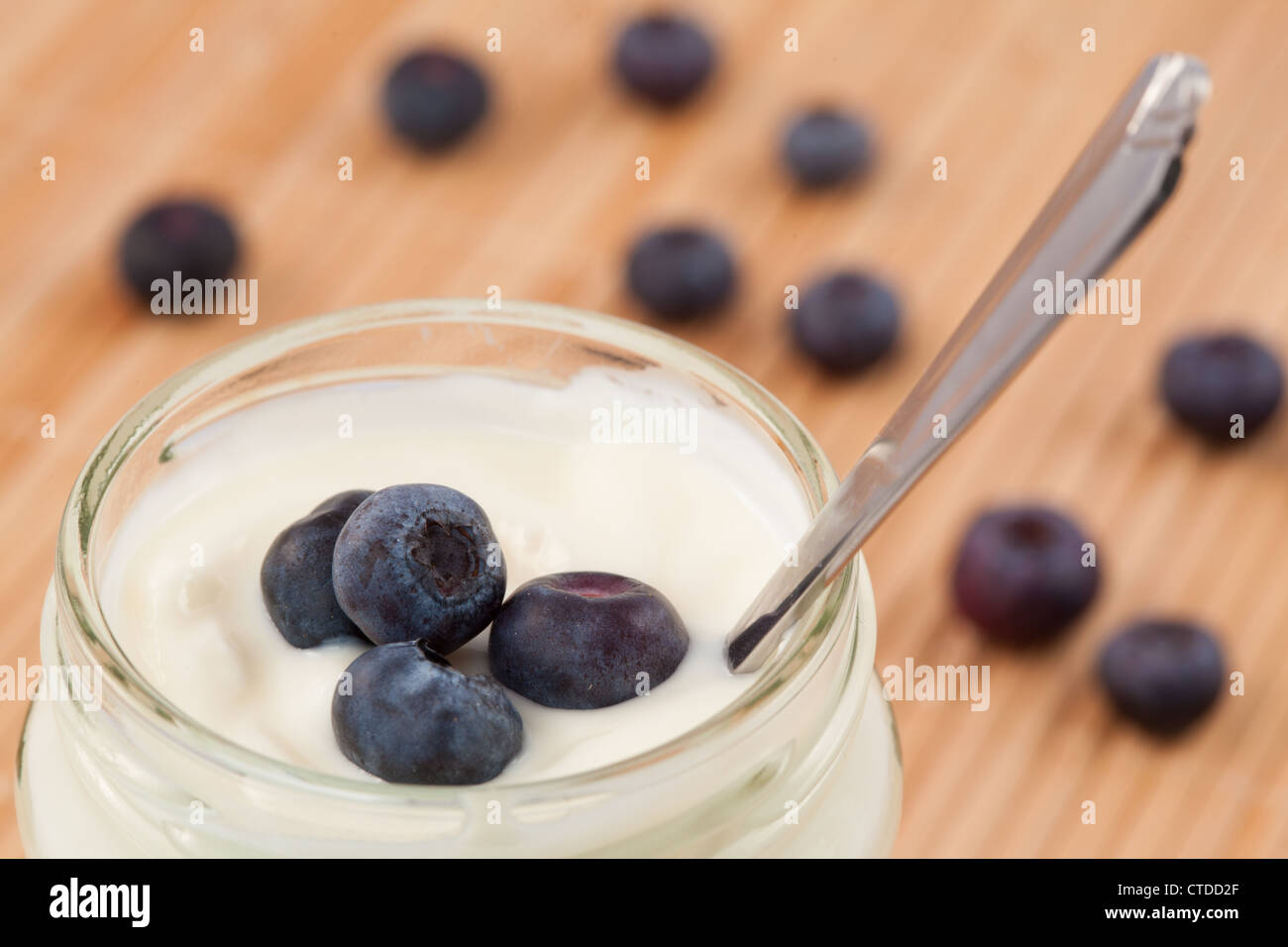 Close up of a pot of yoghurt with blueberries displayed behind Stock Photo
