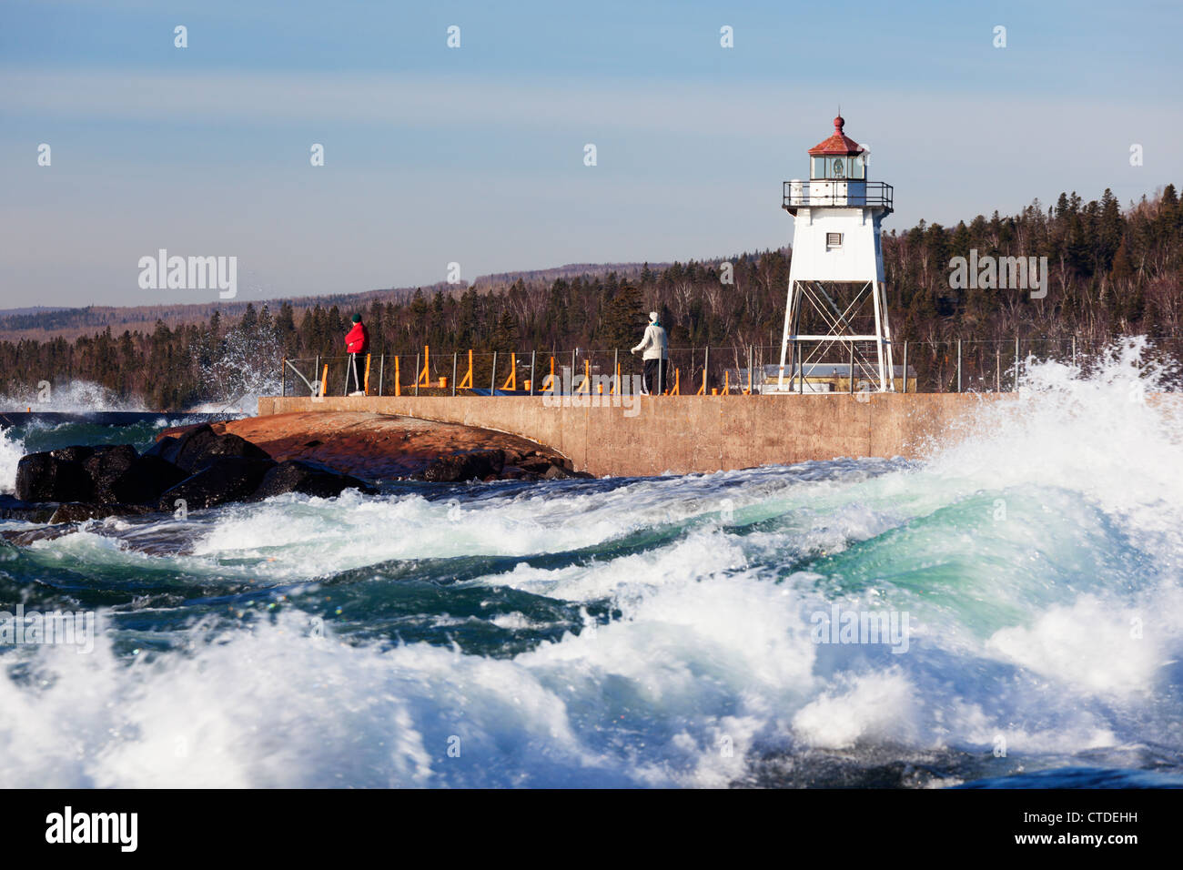 Two people on the breakwater in Grand Marais, Minnesota watch rough Lake Superior waves. Stock Photo