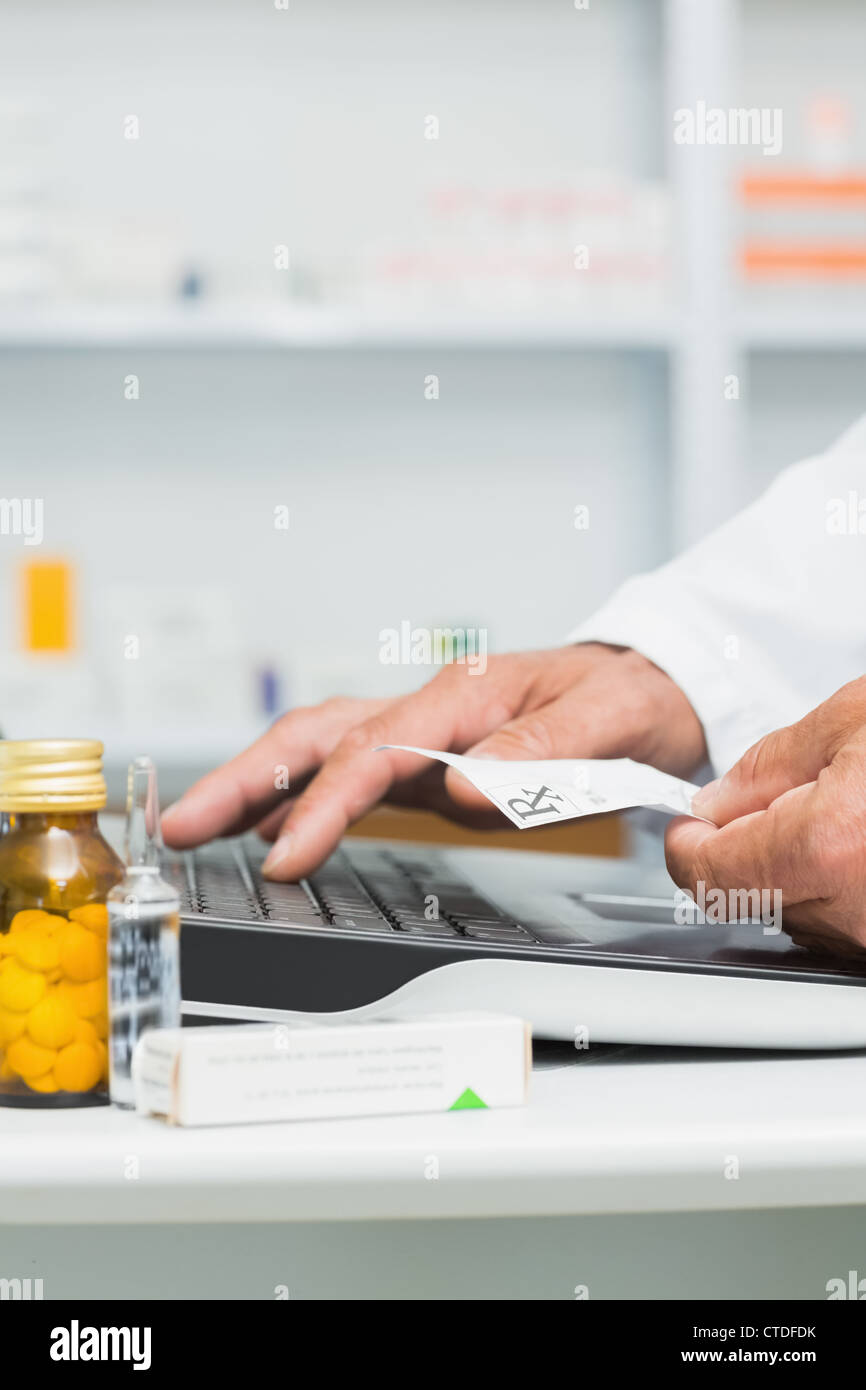Pharmacist holding a prescription while using a computer on a desk Stock Photo
