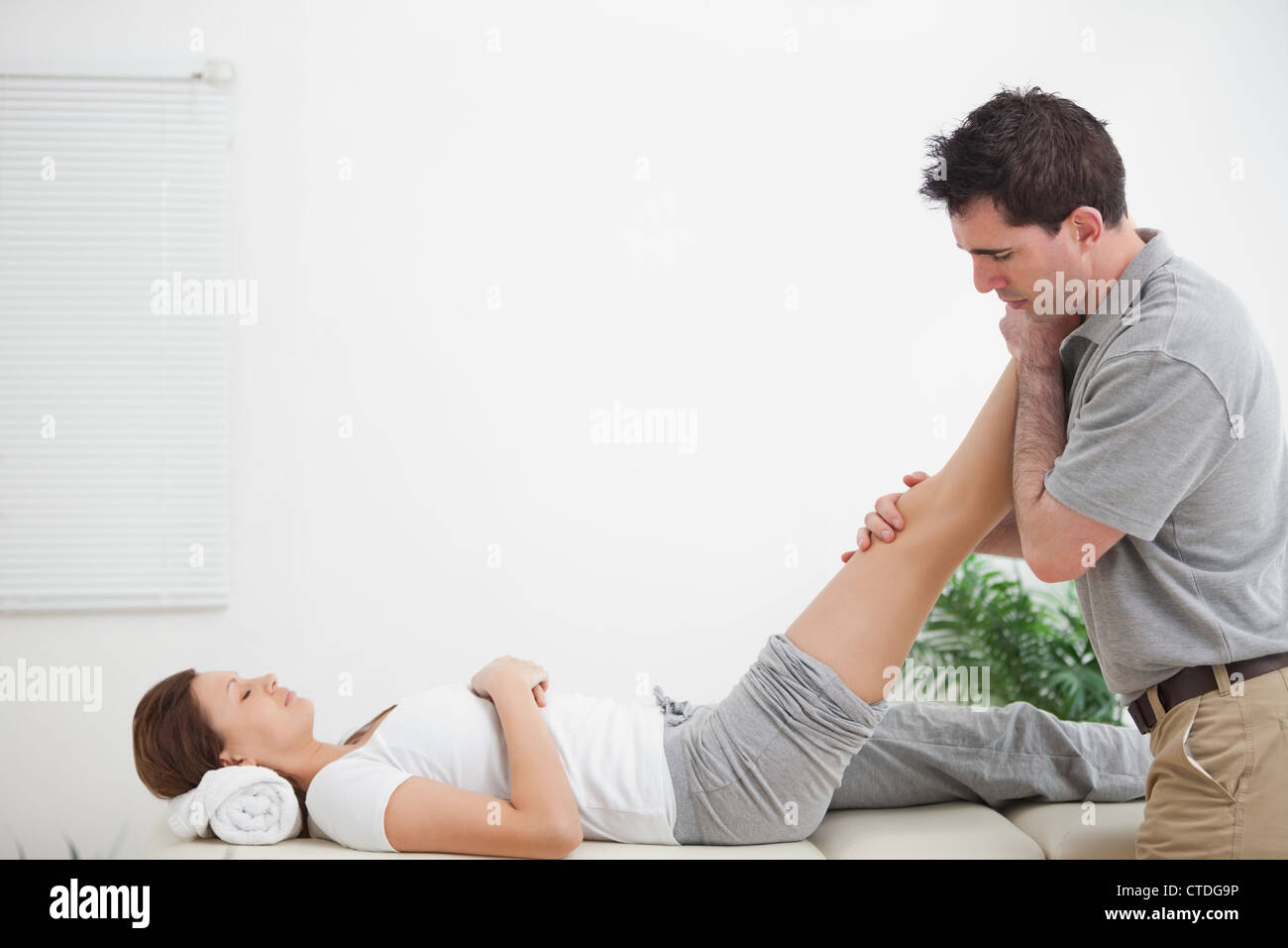 Chiropractor massaging a leg while placing it on his shoulder Stock
