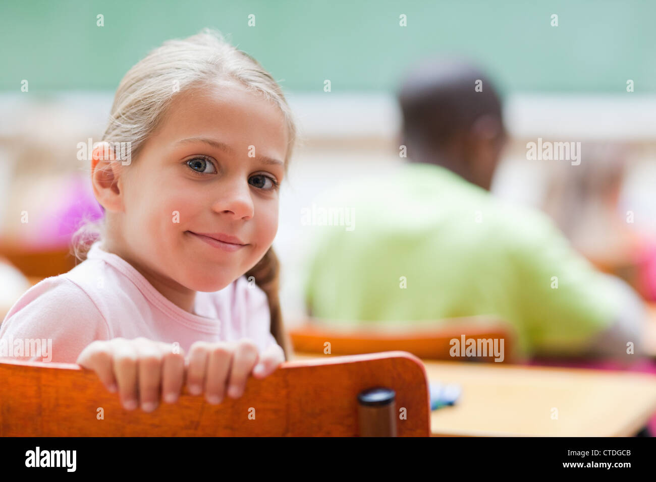 Smiling little girl sitting at school desk Stock Photo - Alamy