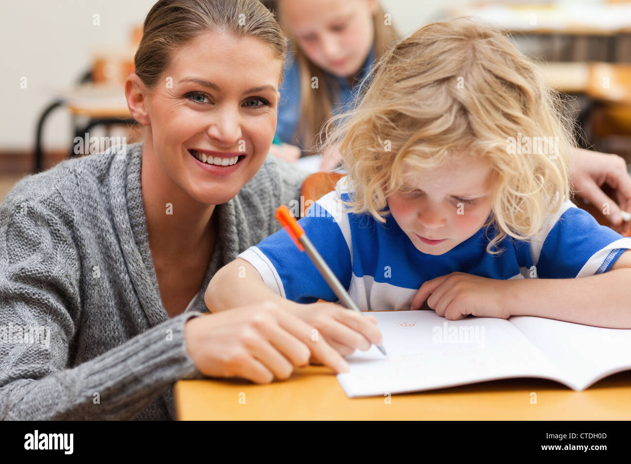 Smiling teacher helping one of her students Stock Photo - Alamy
