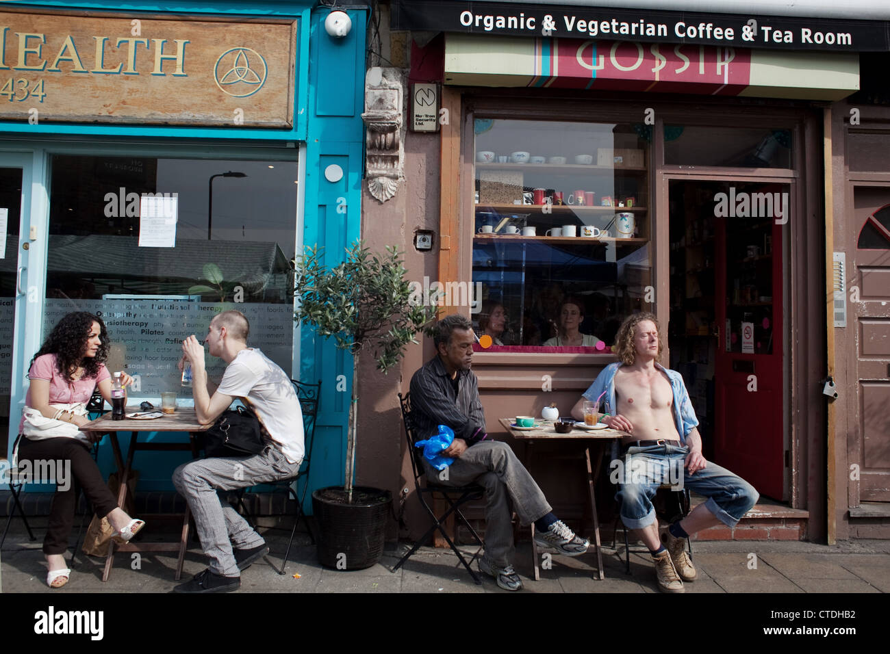 It's a hot day and people relax outside the Holistic Health shop and the vegan coffee shop Gossip. Stock Photo
