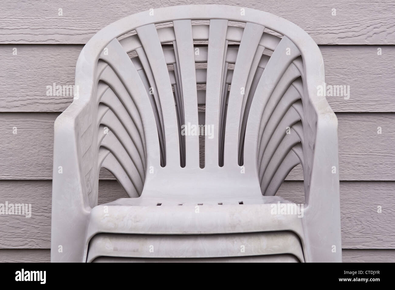 Stacked grey lawn chairs along side of house Stock Photo