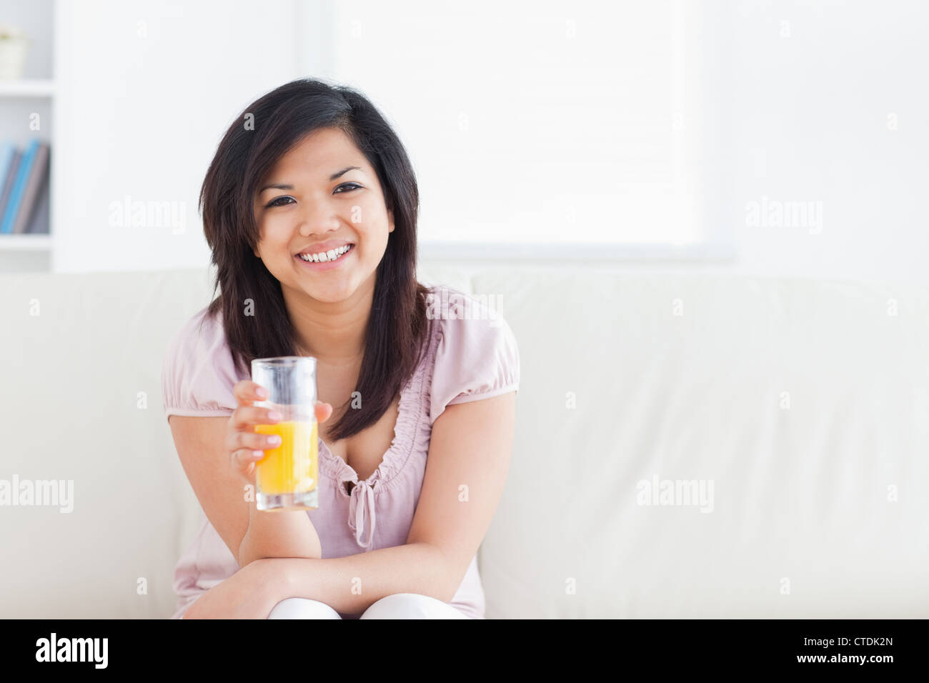 Woman smiling and sitting in a couch while holding a glass of orange juice Stock Photo