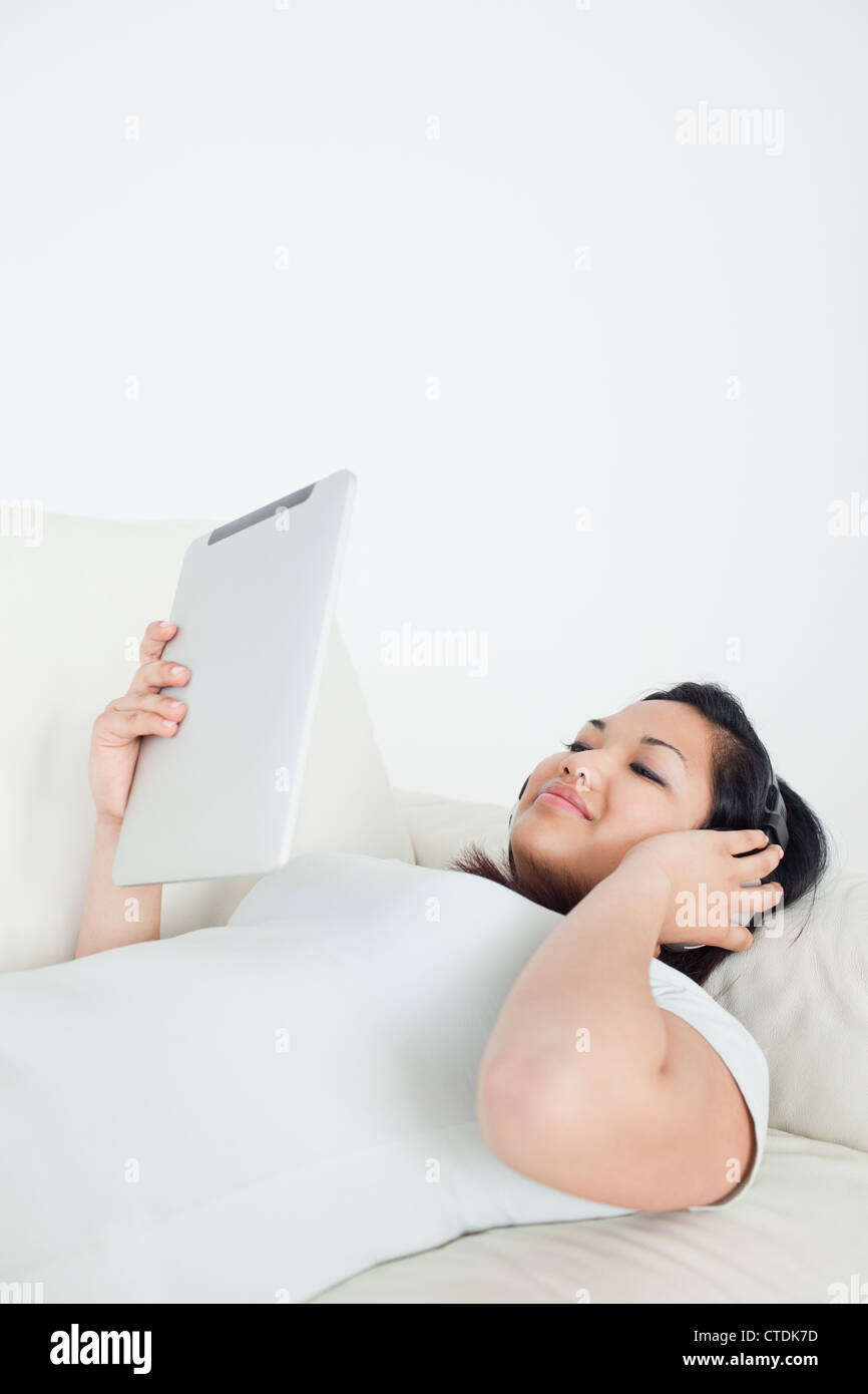 Woman lying on a couch with headphones on and holding a tactile tablet Stock Photo
