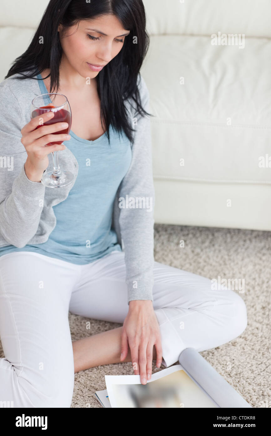 Woman reading a magazine while sitting on a carpet and holding a glass of wine Stock Photo