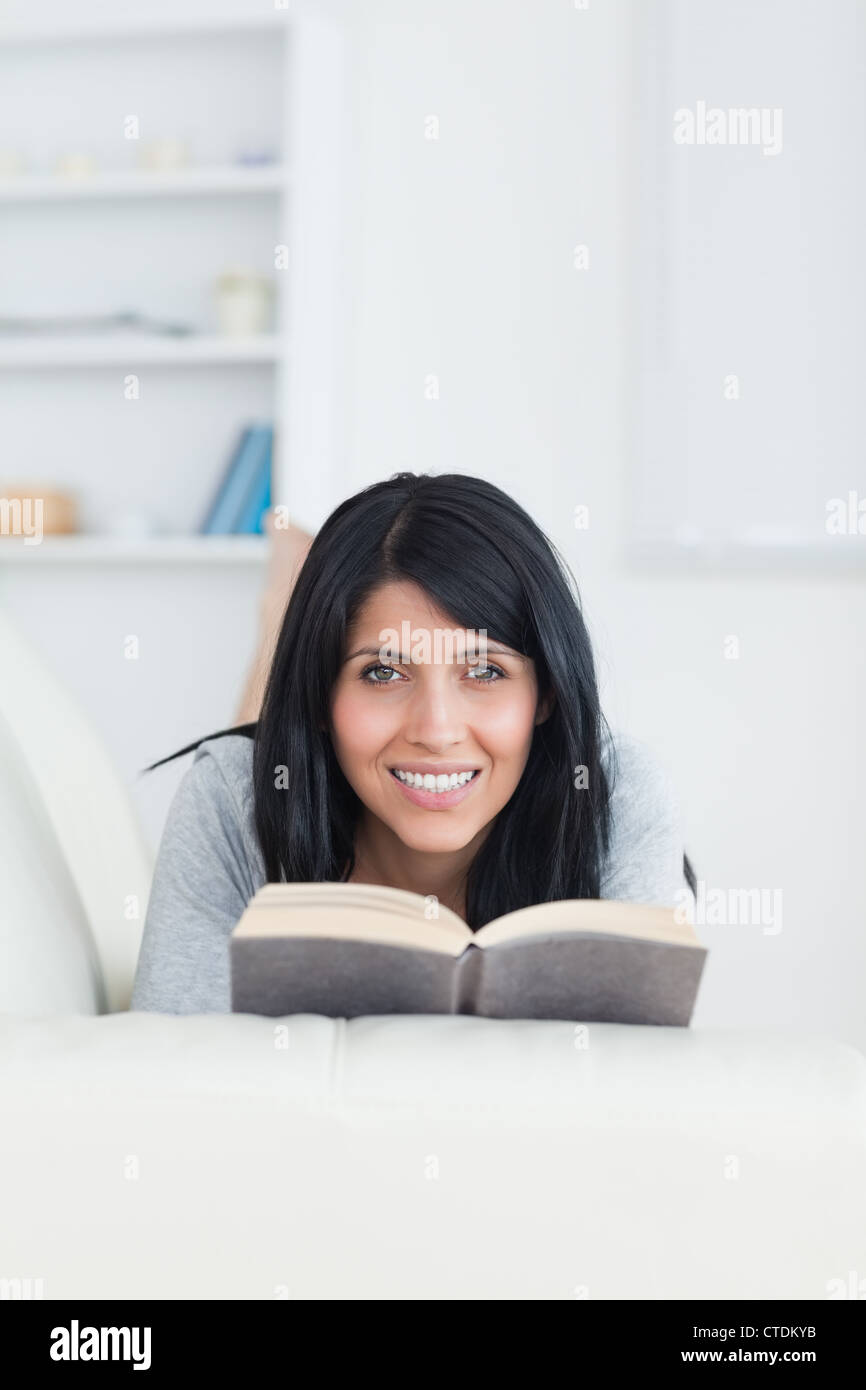 Woman holding a book while smiling and lying on a couch Stock Photo - Alamy