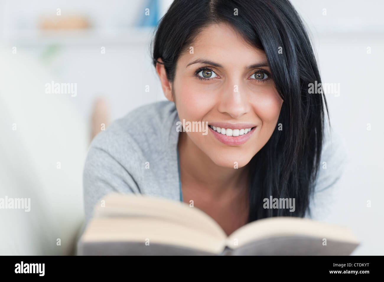 Woman smiling while holding a book in a couch Stock Photo - Alamy