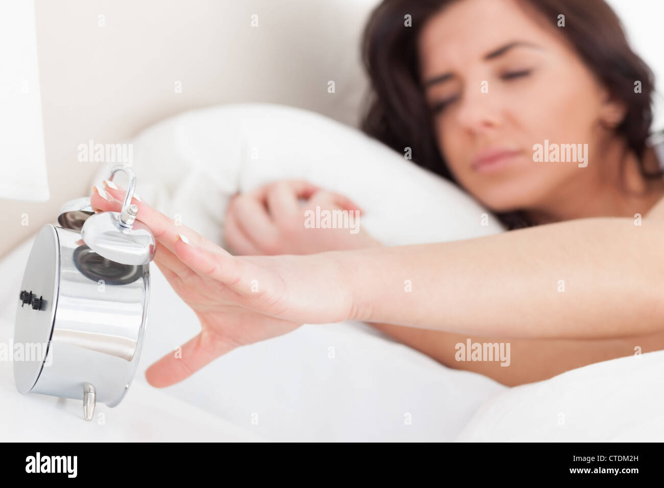 Brunette woman trying to turn off her alarm clock Stock Photo
