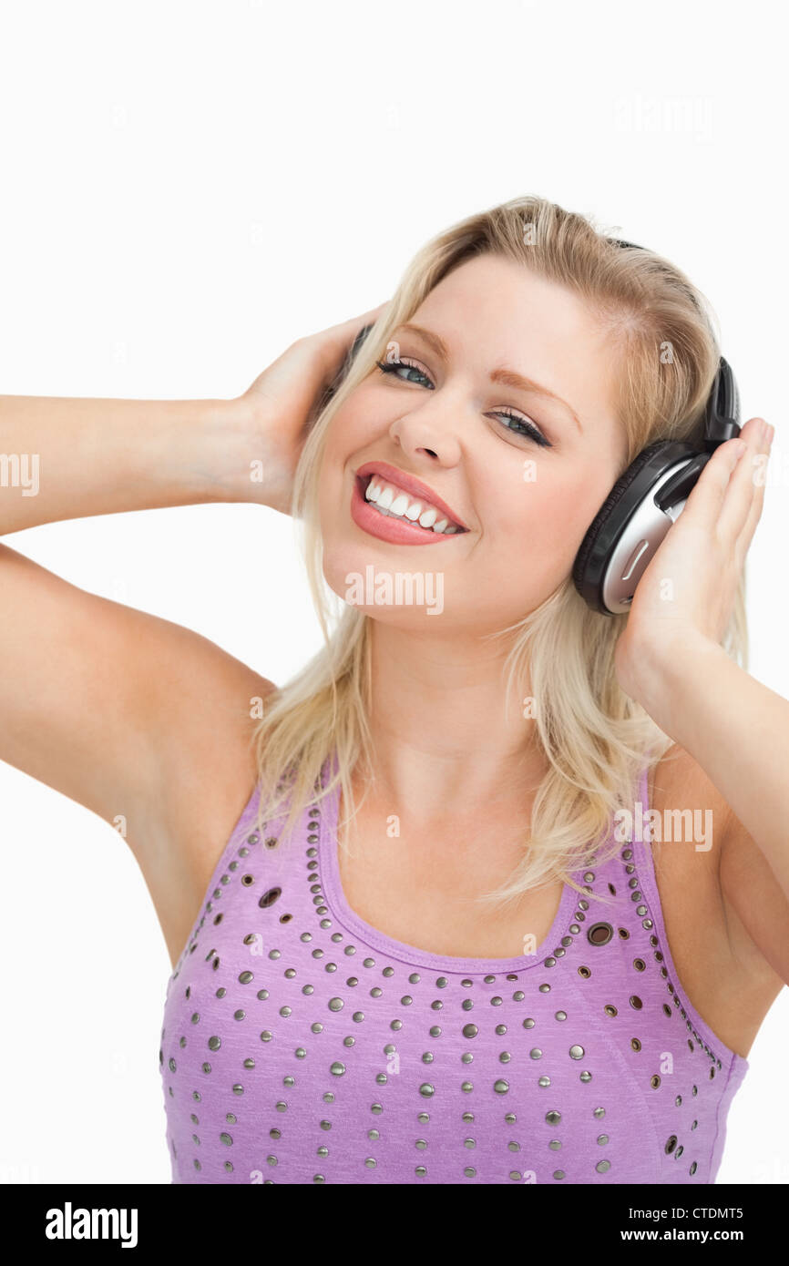 Smiling blonde woman wearing headphones while touching them Stock Photo