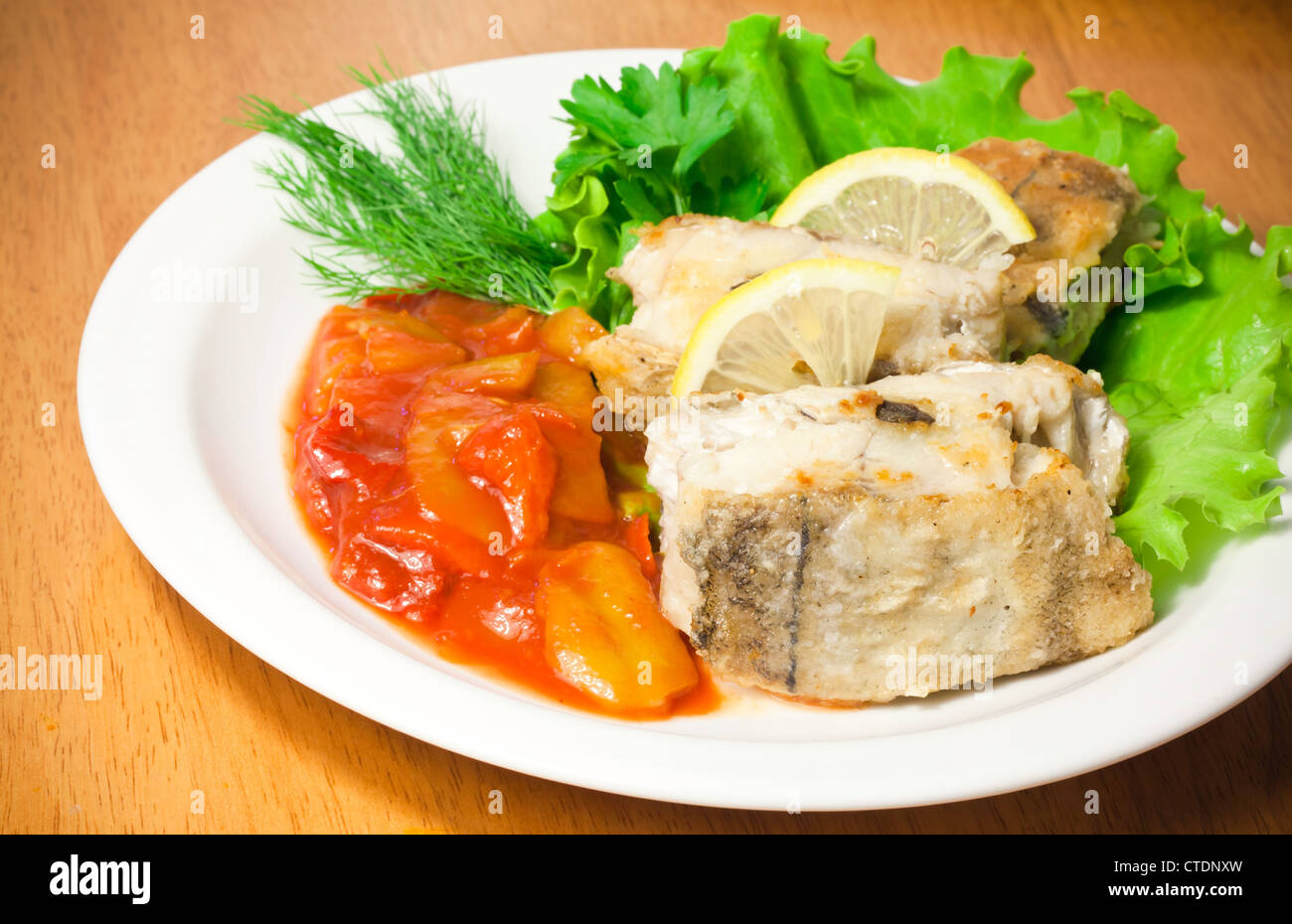 Fried haddock fish with vegetables and greens on white plate Stock Photo