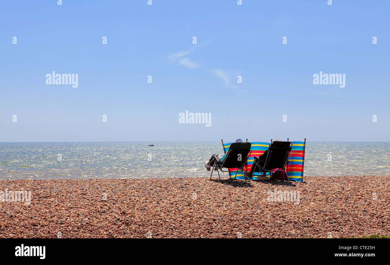 Two people sitting in deckchairs on a beach Stock Photo