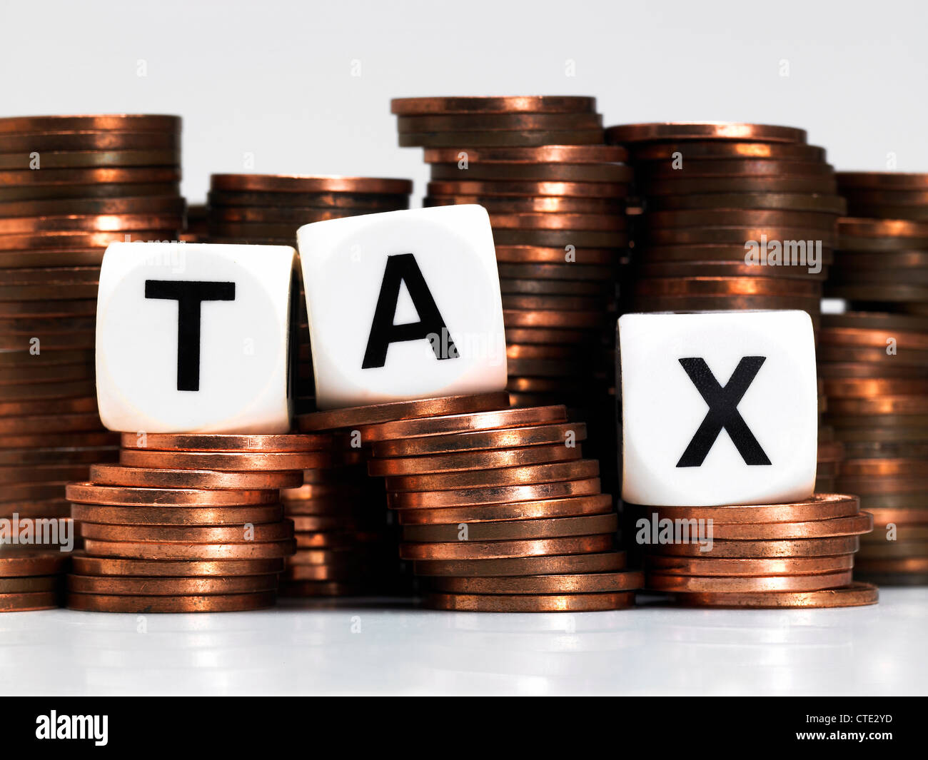 Dice balancing on a pile of coins, spelling out tax Stock Photo