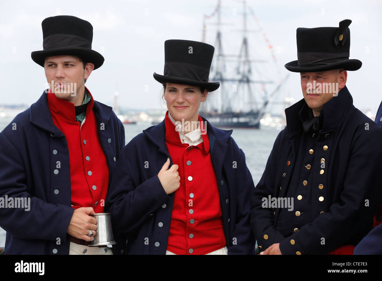 US Coast Guard seamen in 1812 uniforms stand on a pier as the USS Constitution, background sails in Boston Harbor Stock Photo