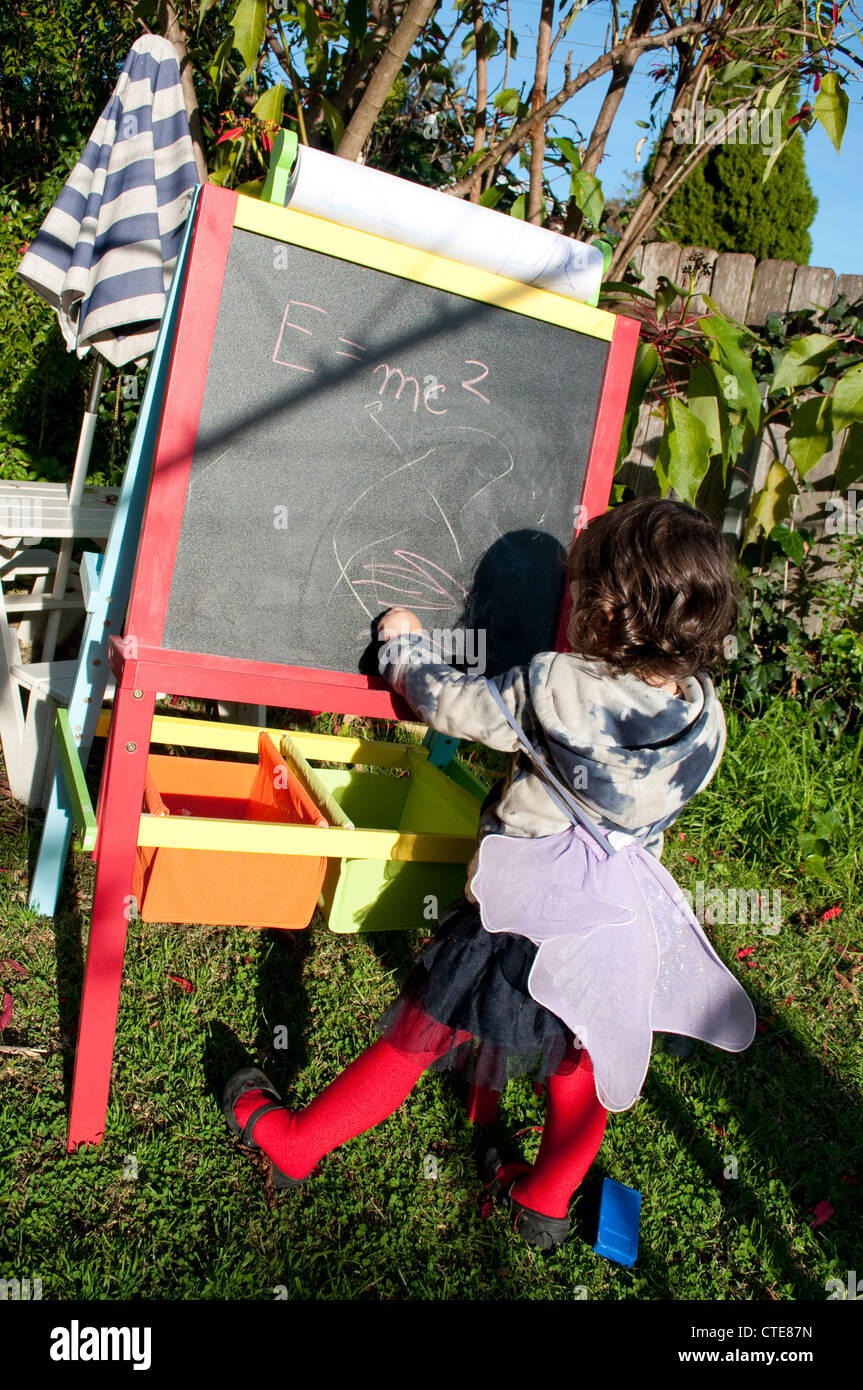 Little girl writing on a blackboard on which is written E = mc2 Stock Photo