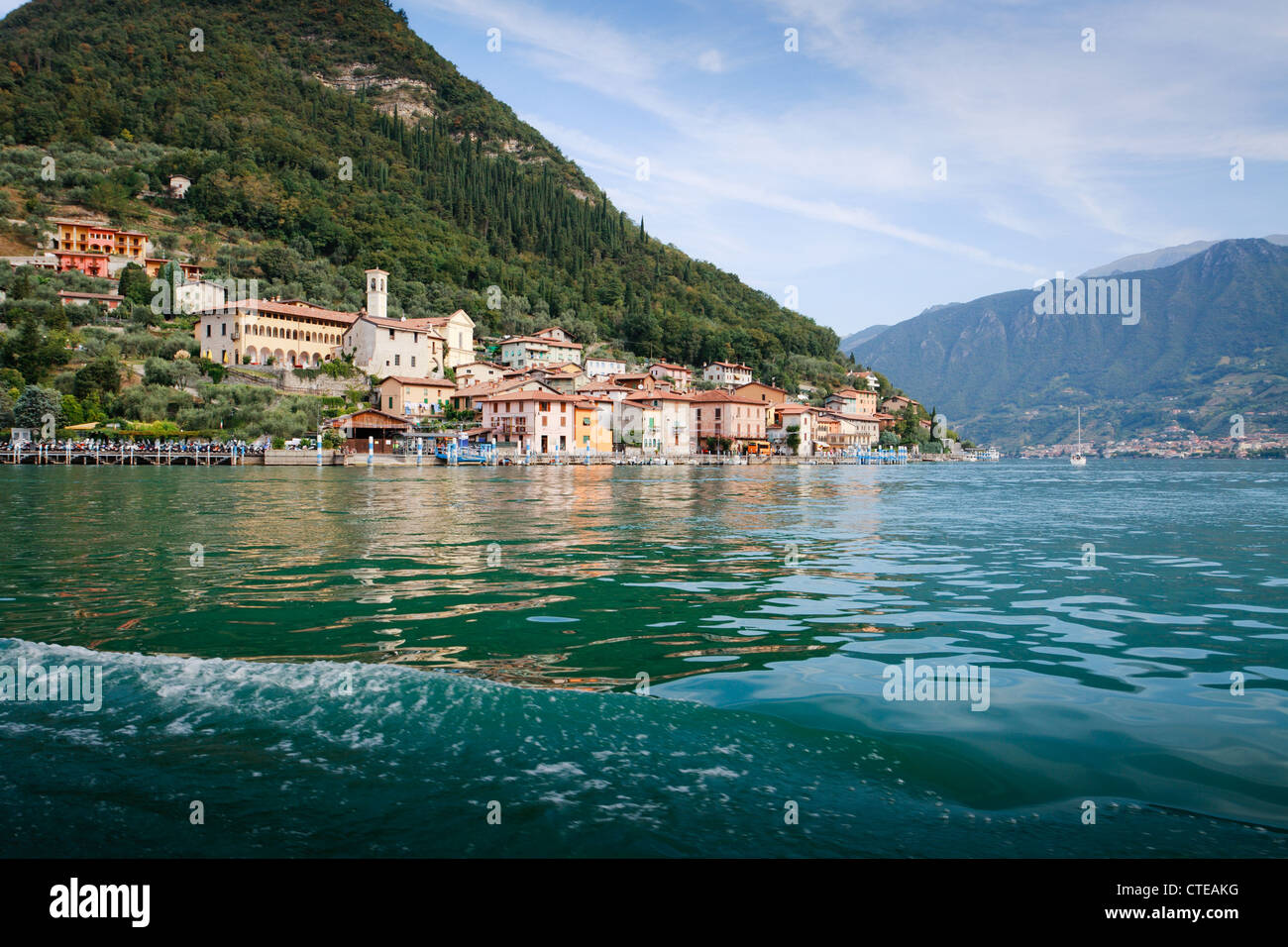 Town of Peschiera, Monte Isola, viewed from boat from Sulzano, with steep hill behind and reflection in water. Stock Photo
