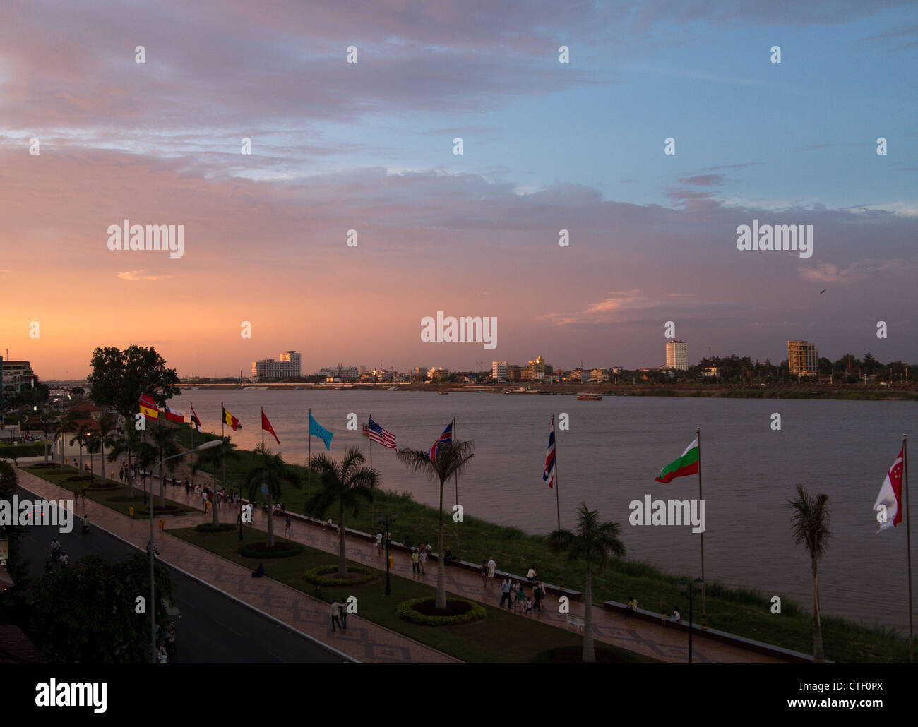 River front of Phnom Penh by Mekong river at dusk with sun setting and people walking along the edge of the water Stock Photo