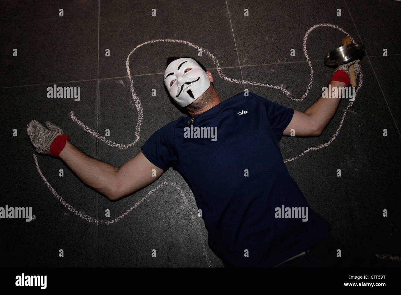 A members of the group Anonymous wearing Guy Fawkes mask laying on the ground in front of a financial building during Cost of Living protest in Tel Aviv Israel. The Guy Fawkes mask is a well-known symbol for the online hacktivist group Anonymous used in anti-government and anti-establishment protests around the world. Stock Photo