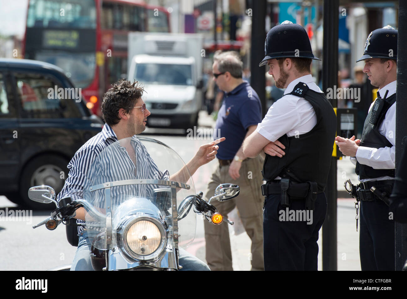 Biker on his Harley Davidson motorcycle not wearing a helmet talking to policemen. Camden high street. London Stock Photo