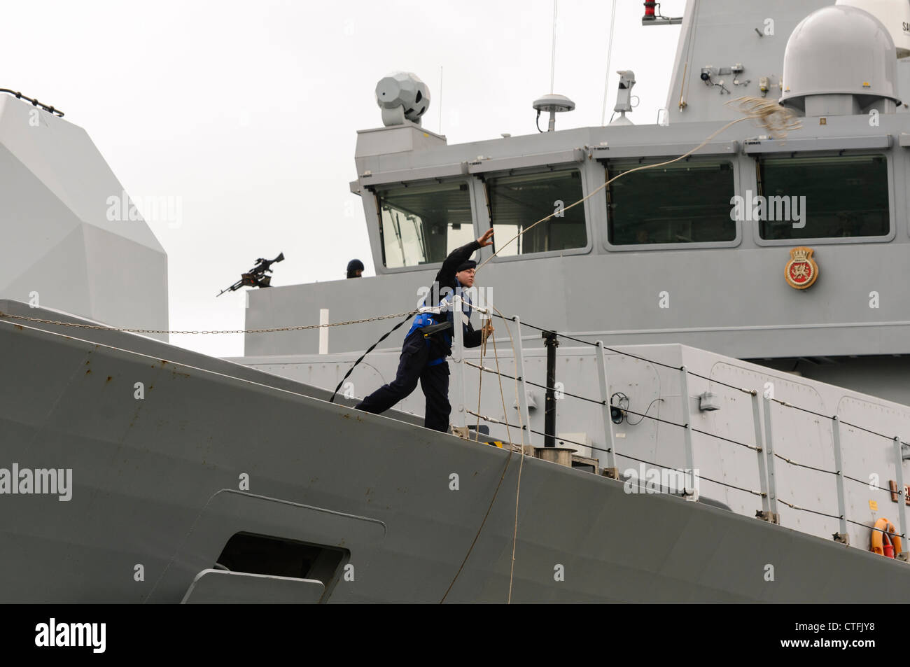 Sailor on Royal Navy Type 45 destroyer HMS Dragon throws a lead rope to dockers Stock Photo