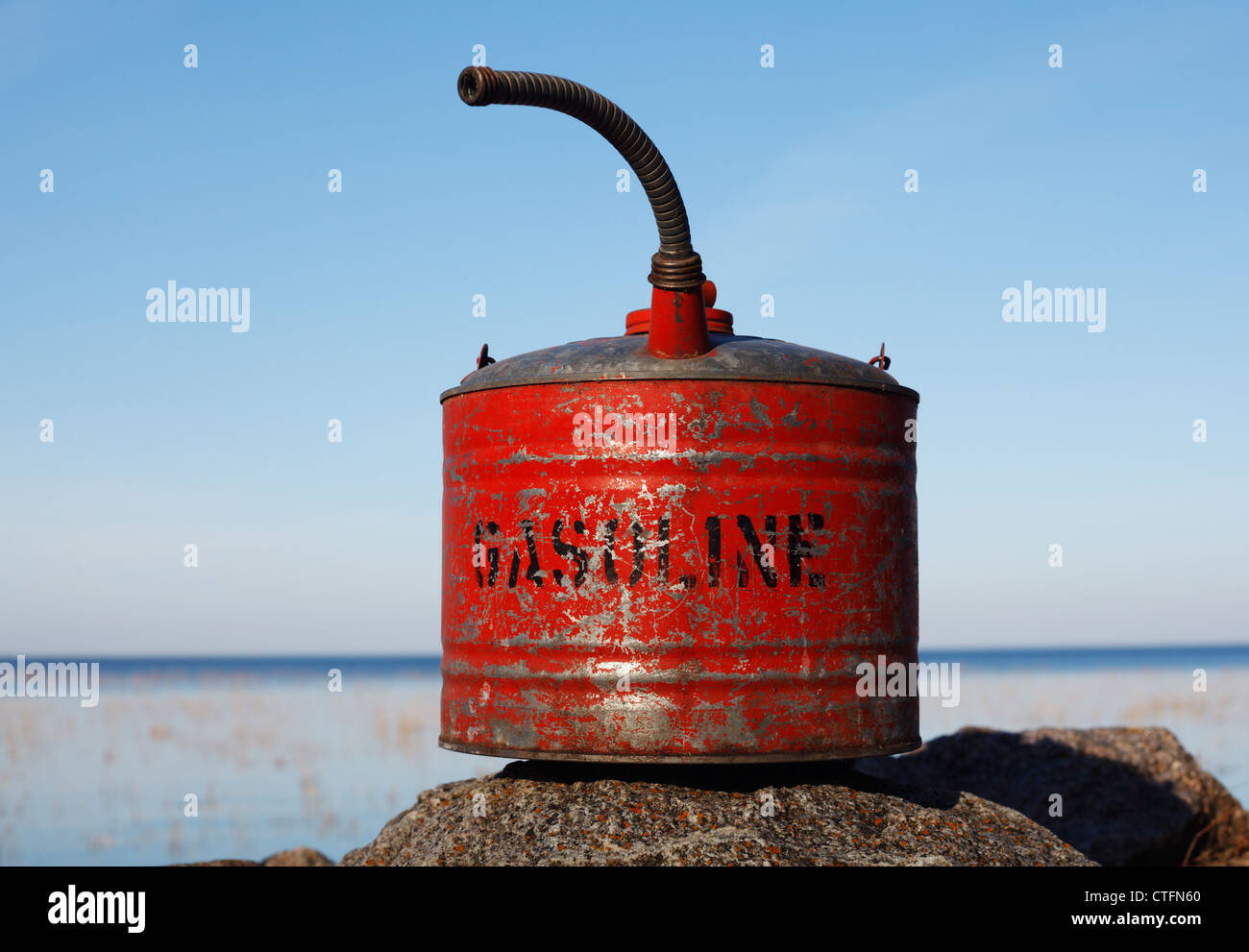 An old, red gasoline can sitting on a rock. Stock Photo