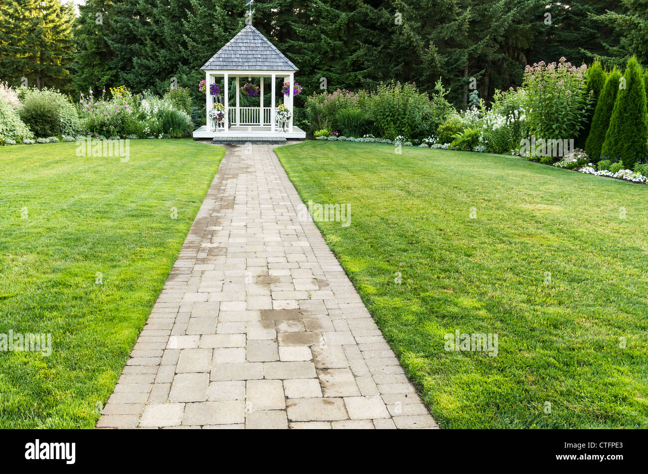 A white wedding gazebo on green lawn at the end of a stone pathway Stock Photo