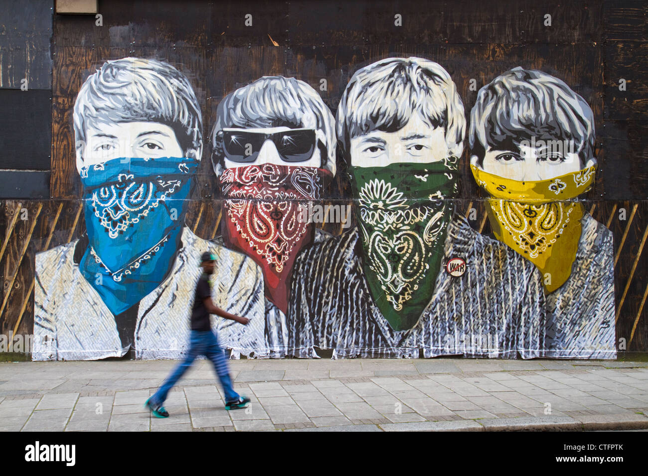 A man walks by a paste-up by street artist Mr Brainwash in London depicting The Beatles wearing face masks. Stock Photo