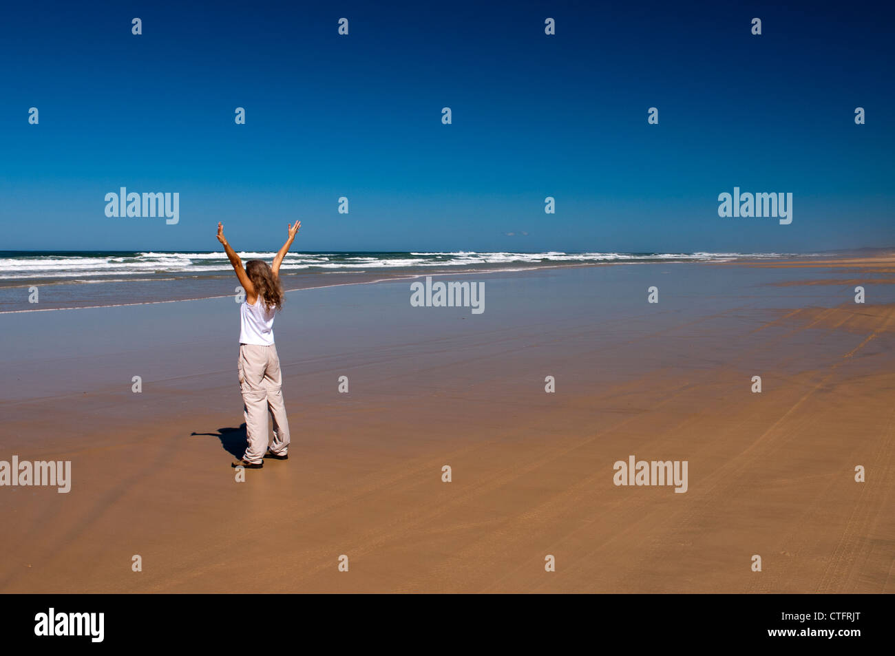 Woman standing alone on a beach on a bright sunny day. Stock Photo