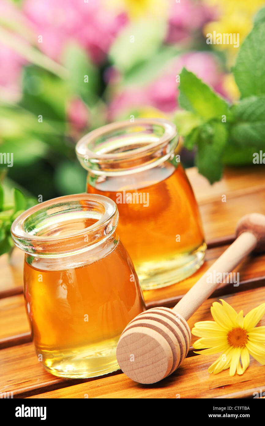 Honey in glass jars with flowers background. Stock Photo
