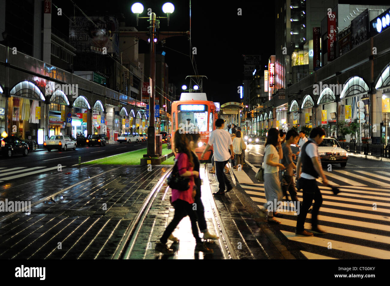 Pedestrians walk in front of a tram in Kagoshima, Japan Stock Photo