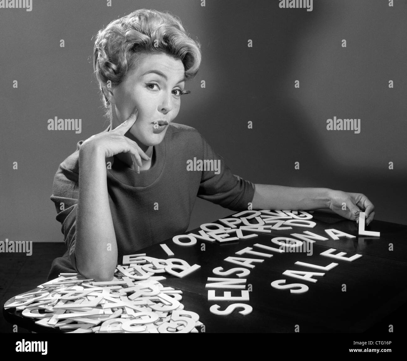 1950s 1960s PORTRAIT BLONDE WOMAN LOOKING AT CAMERA SPELLING OUT SENSATIONAL SALE WITH CUTOUT GRAPHIC DESIGN  LETTERS Stock Photo