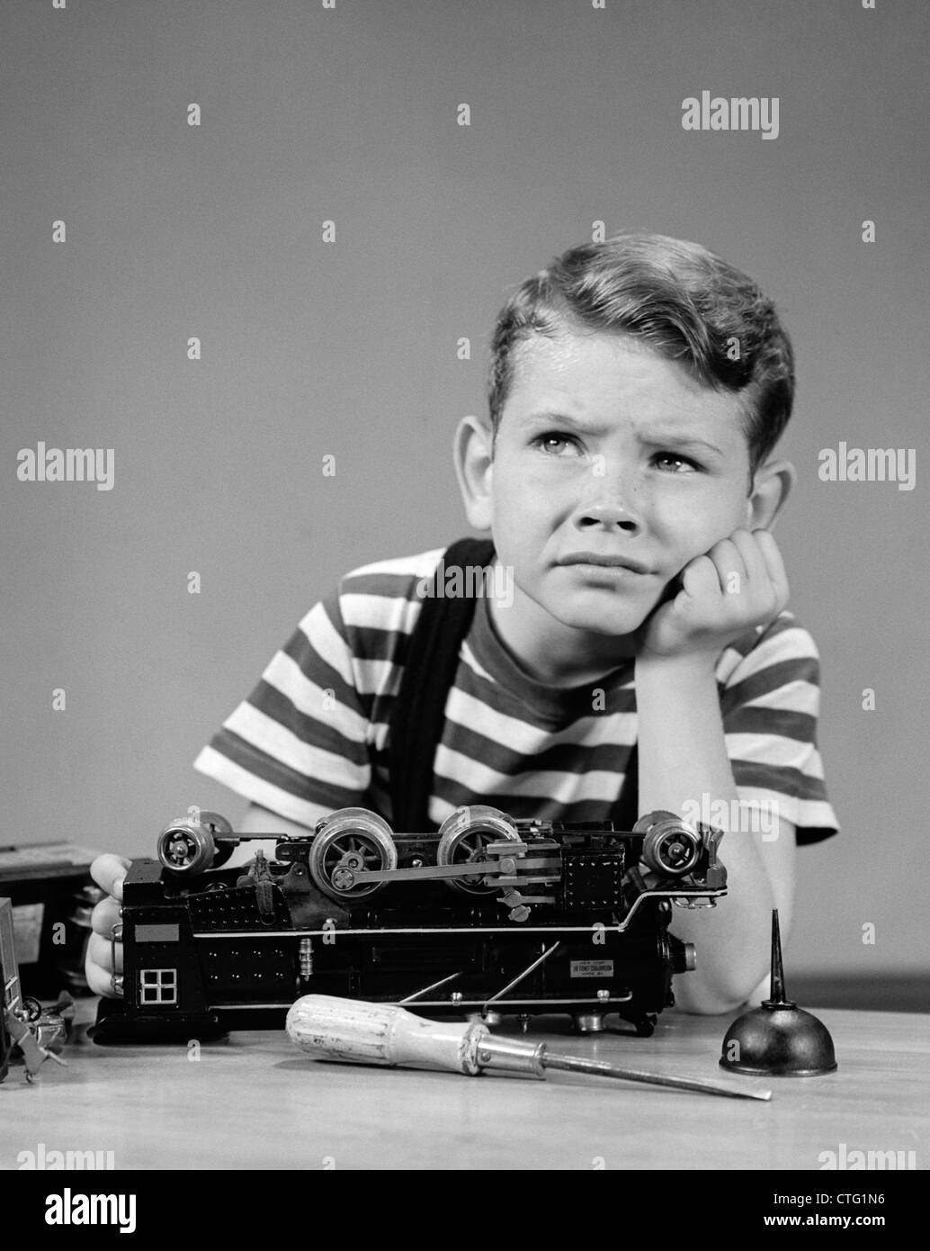 1930s 1940s LITTLE BOY THINKING OR WORRYING ABOUT BROKEN LIONEL ELECTRIC TOY TRAIN ENGINE Stock Photo