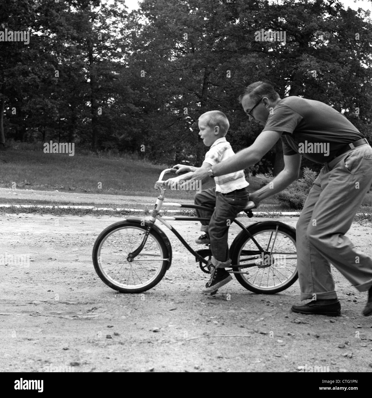 1960s FATHER GIVING SON ON BIKE A PUSH TEACHING HIM HOW TO RIDE BICYCLE Stock Photo