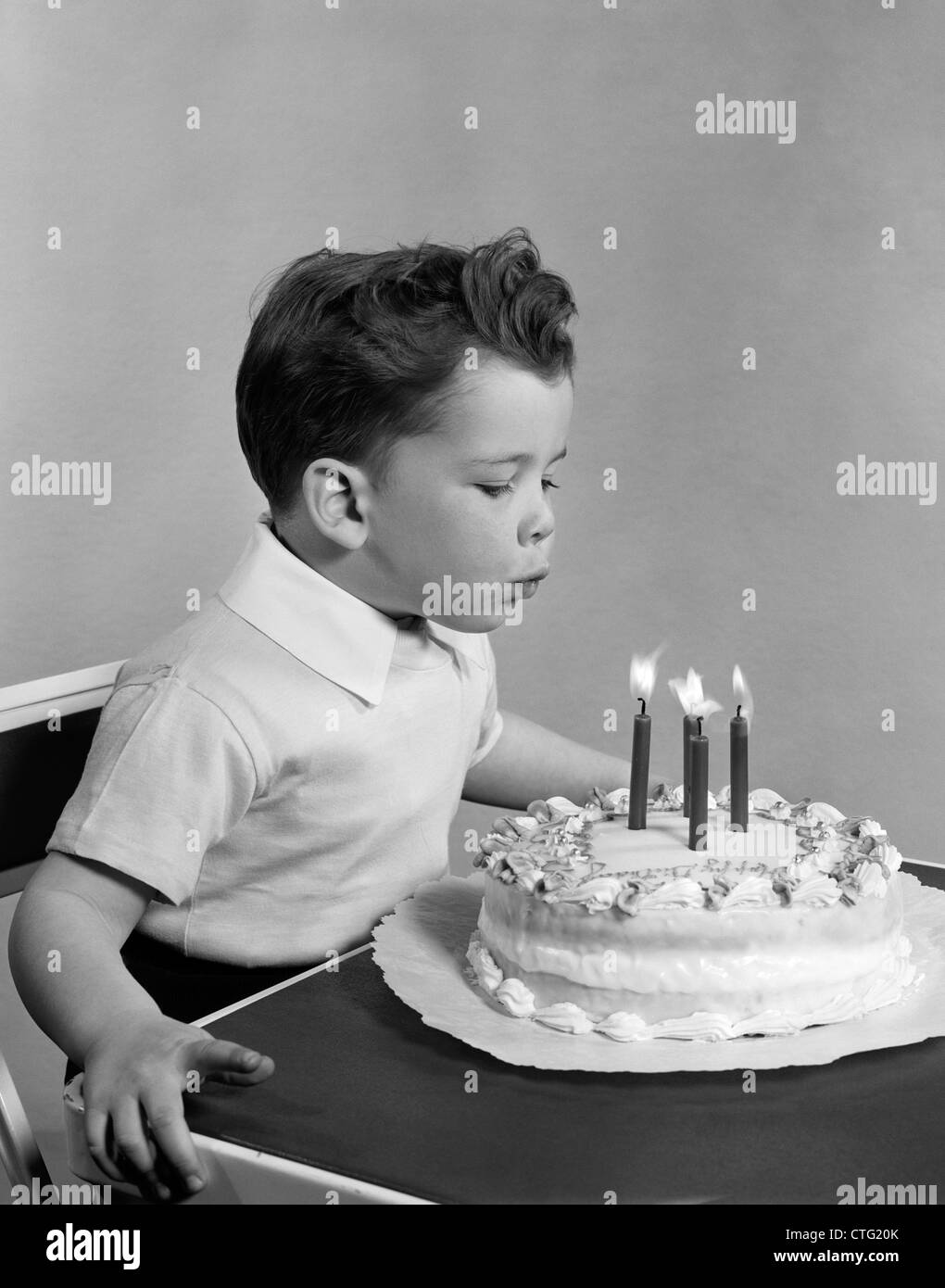 1950s BOY FOUR YEARS OLD BLOWING OUT CANDLES ON BIRTHDAY CAKE INDOOR Stock Photo