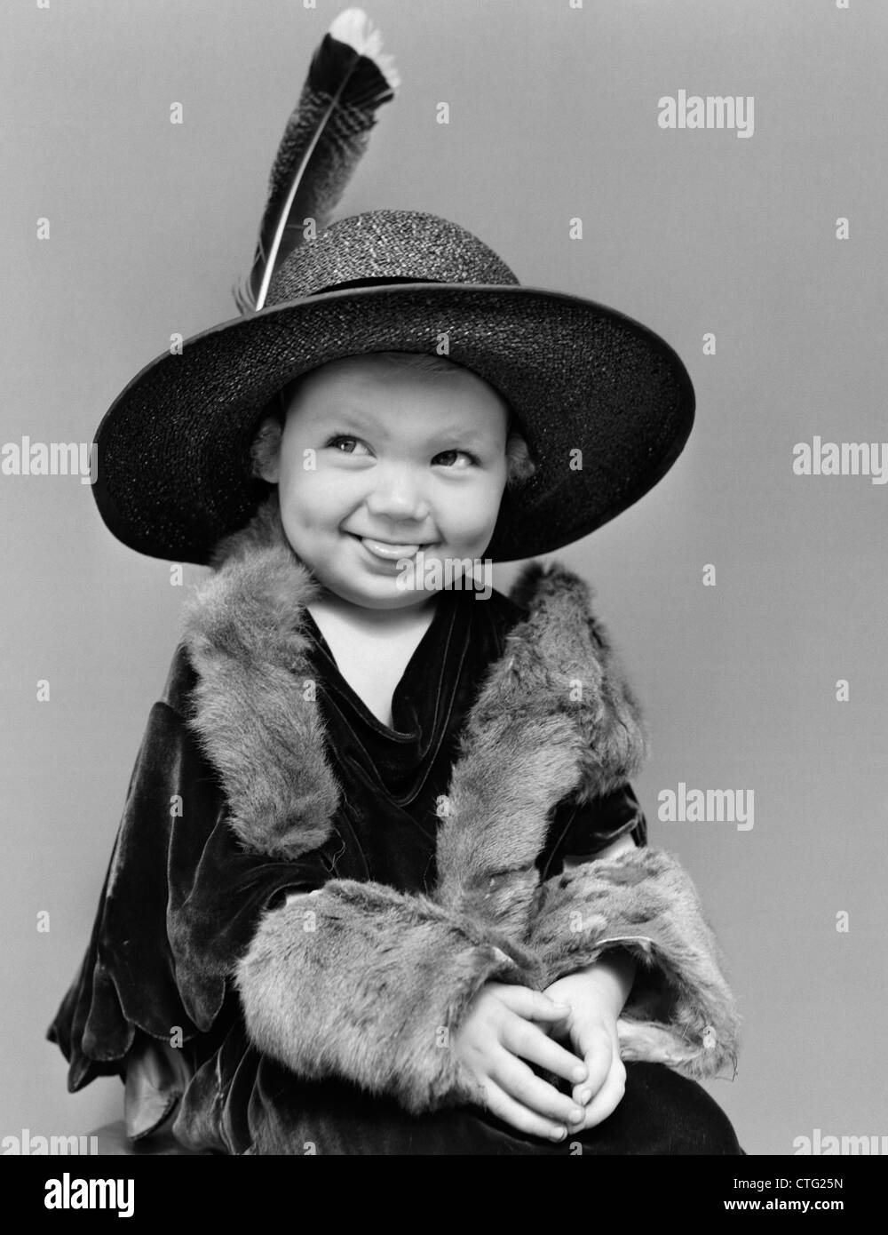 1940s GIRL IN OVERSIZED VELVET DRESS HAT & FURS WITH EYES CAST TO SIDE & TONGUE STICKING PARTIALLY OUT Stock Photo