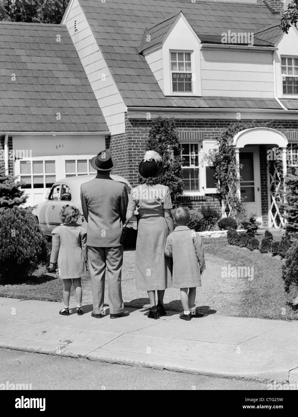 1940s FAMILY MOTHER FATHER DAUGHTER SON LOOKING AT SUBURBAN HOUSE BACK VIEW OUTDOOR Stock Photo