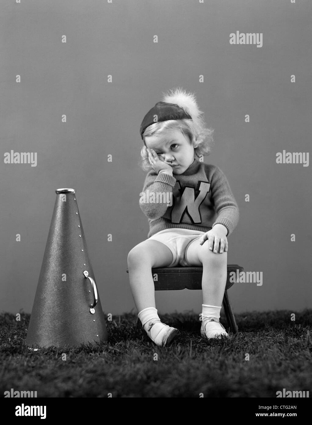 1940s UNHAPPY LITTLE GIRL CHEERLEADER WEARING A CAP AND VARSITY SWEATER FRUSTRATED SAD LOOK Stock Photo