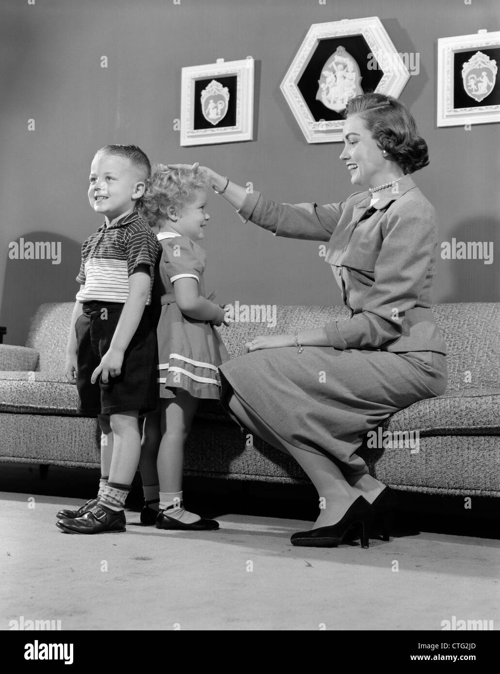1950s MOTHER MEASURING DIFFERENCE IN HEIGHT BETWEEN SON AND DAUGHTER INDOOR Stock Photo