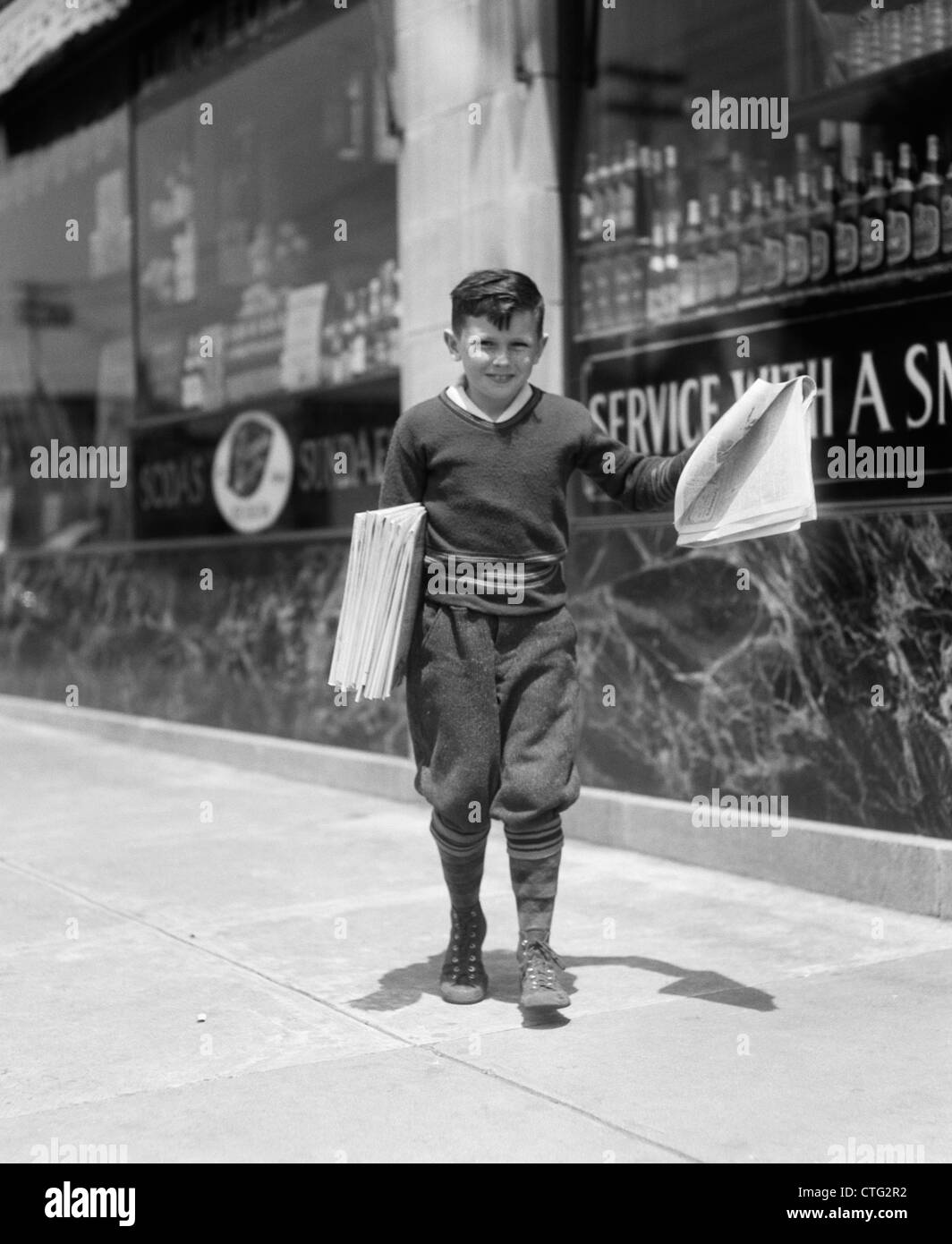 1930s NEWSBOY IN KNICKERS WALKING DOWN STREET HAWKING PAPERS Stock Photo