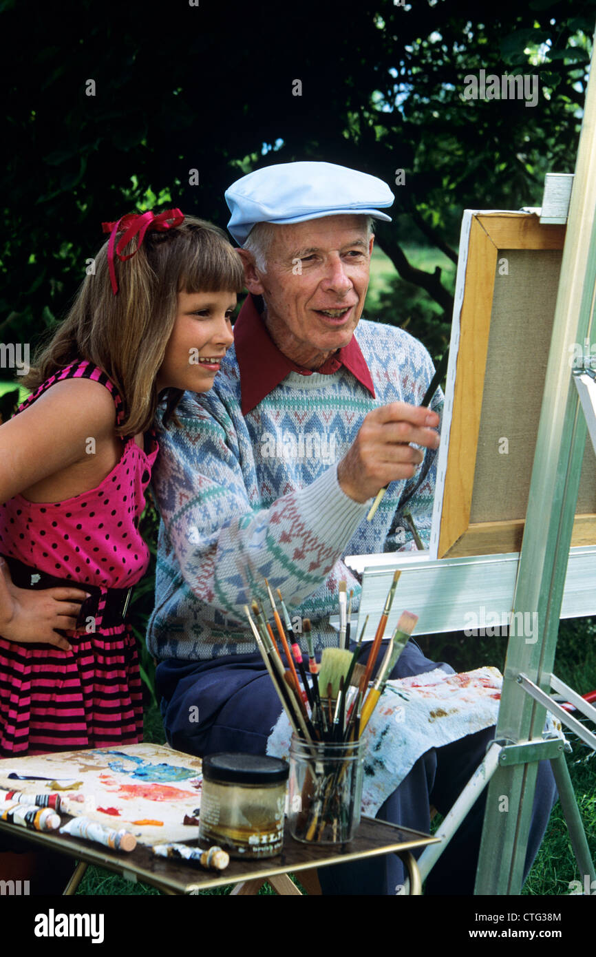 1980s 1990s GRANDDAUGHTER WATCHING GRANDFATHER PAINT AT EASEL Stock Photo