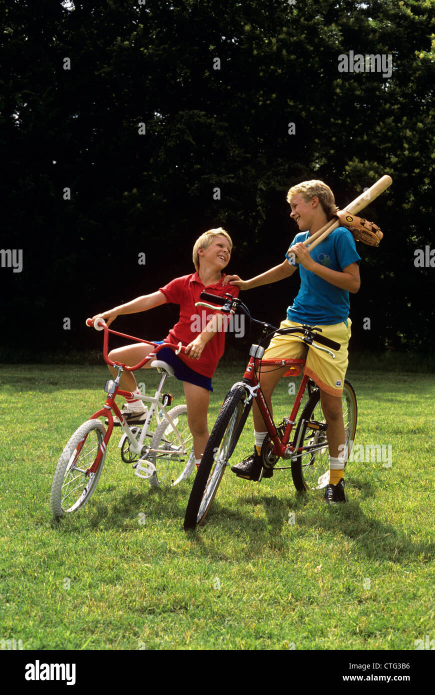 1980s 1990s JUVENILE BOY AND TEENAGE BOY ON BICYCLES WITH BASEBALL BAT AND GLOVE Stock Photo
