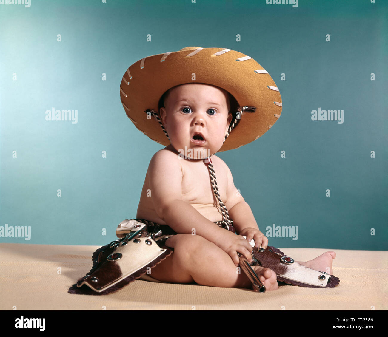 1960s BABY WEARING COWBOY COSTUME WITH FUNNY FACIAL EXPRESSION LOOKING AT CAMERA Stock Photo