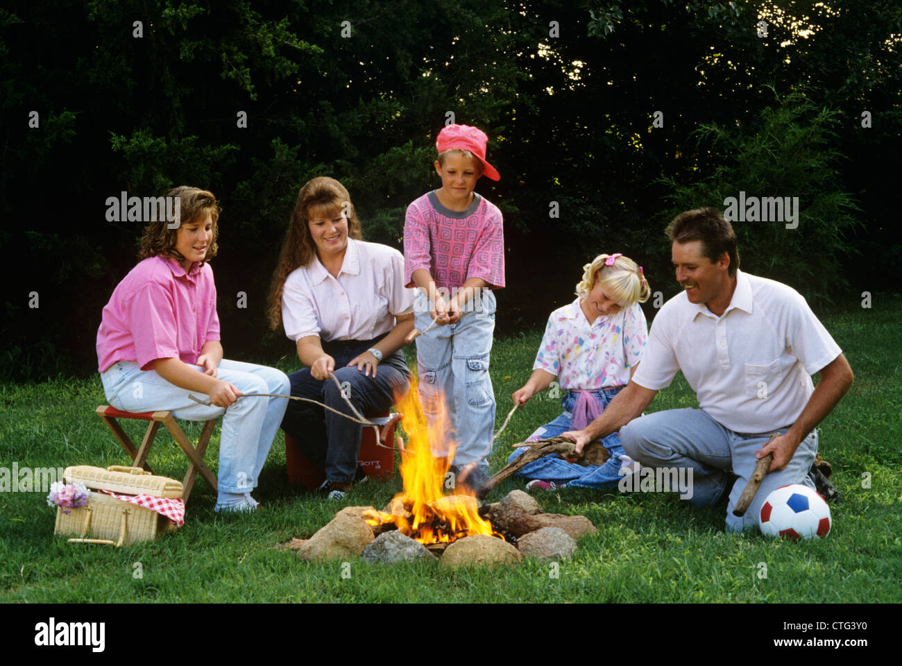 1990s FAMILY ROASTING HOT DOGS ON STICKS OVER CAMPFIRE Stock Photo