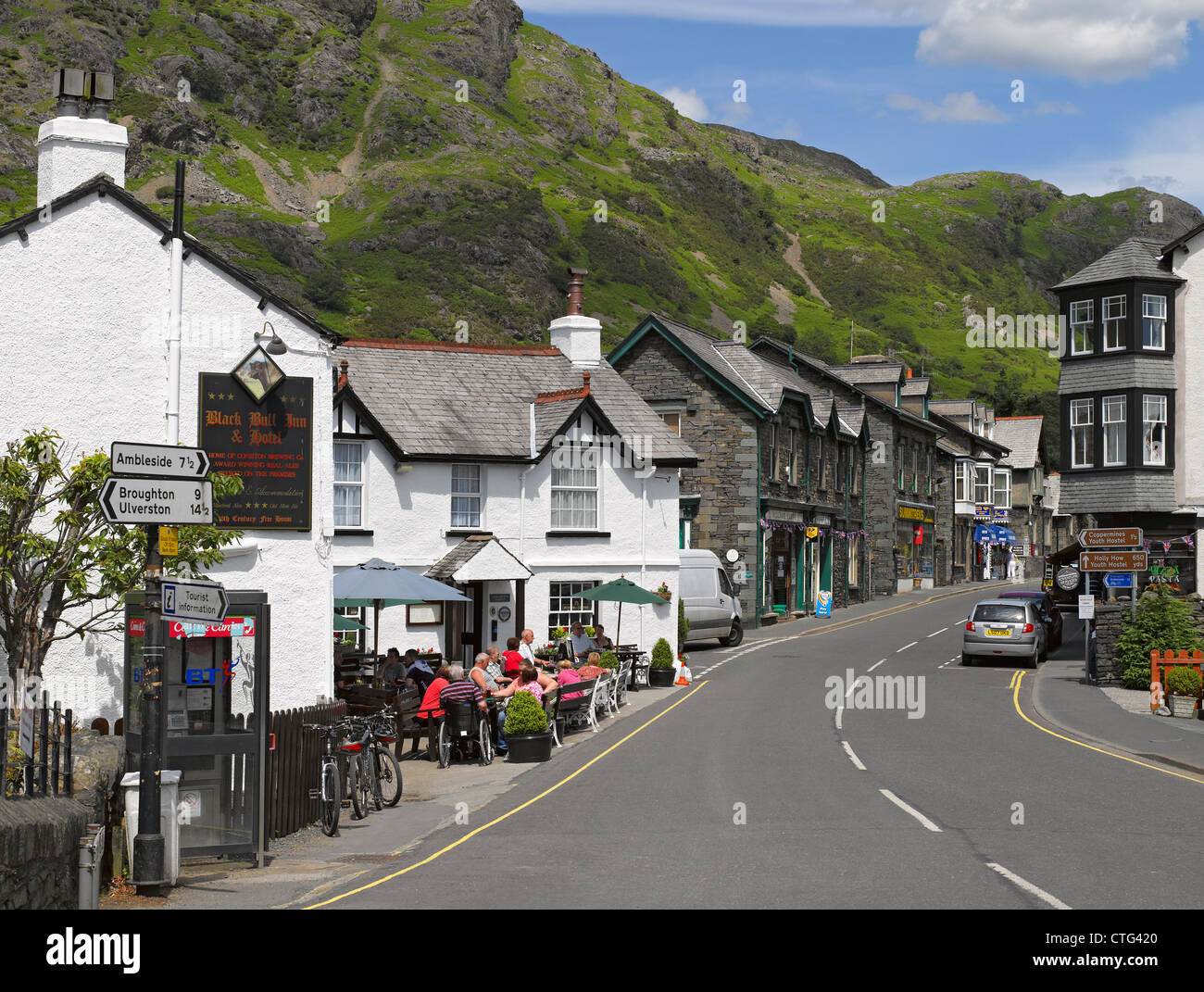 People tourist visitors outside the Black Bull Inn pub shops and cottages summer Coniston village Cumbria England UK United Kingdom GB Great Britain Stock Photo