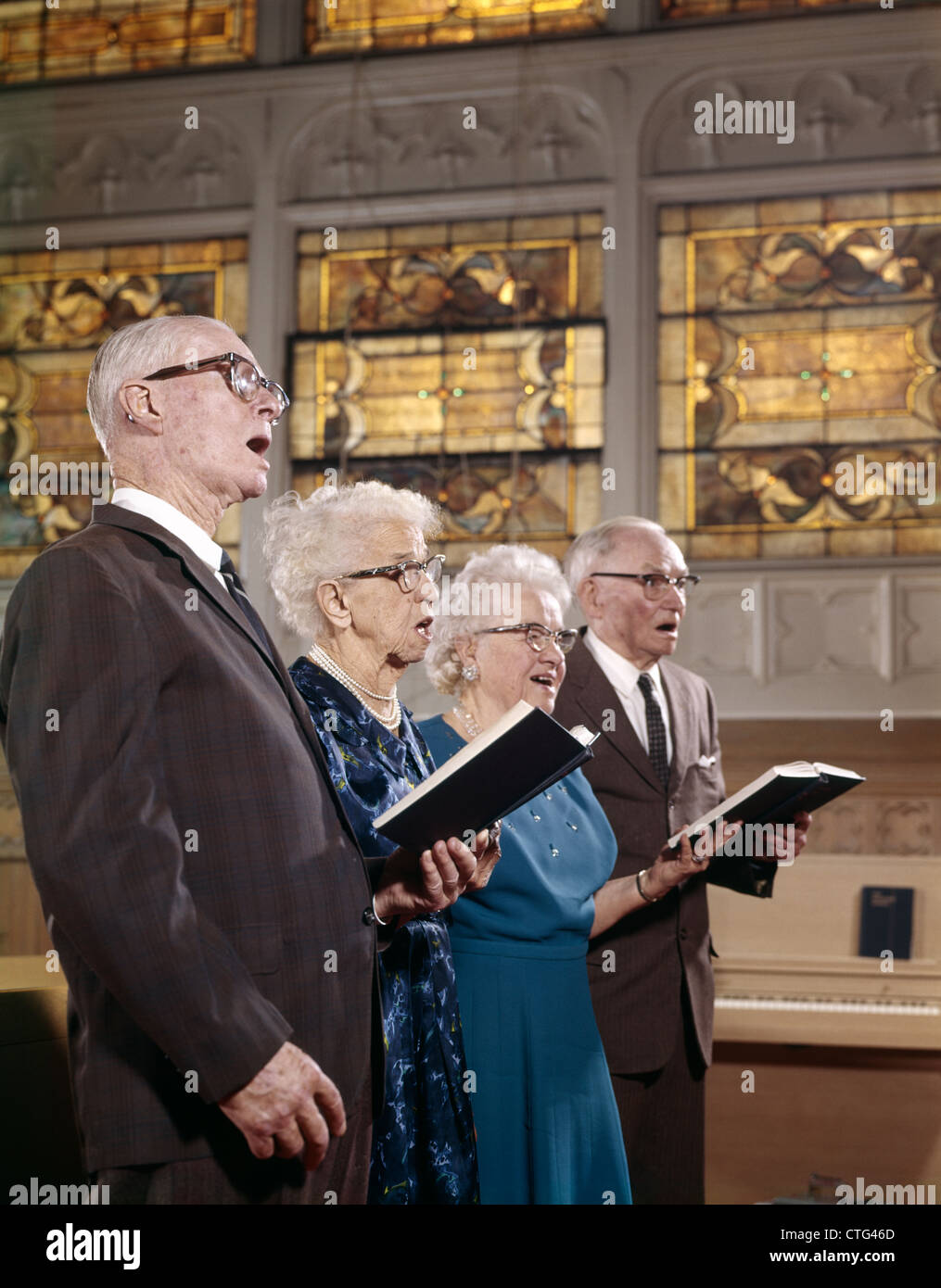 1960s TWO ELDERLY COUPLES IN CHURCH SINGING FROM HYMNAL BOOKS Stock Photo