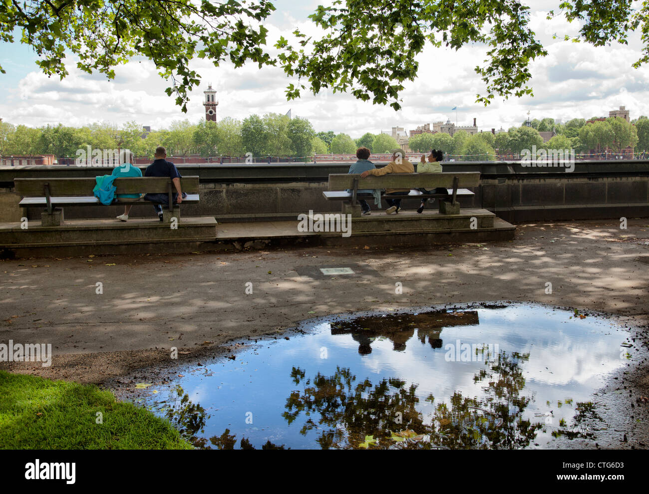 Victoria Gardens People on bench and trees reflected in puddle - London UK Stock Photo